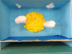 premier prix defi art ecole sainte marie fuveau un soleil en papier relief, des nuages suspendus sur fond bleus présentés dans une boîte à chaussues